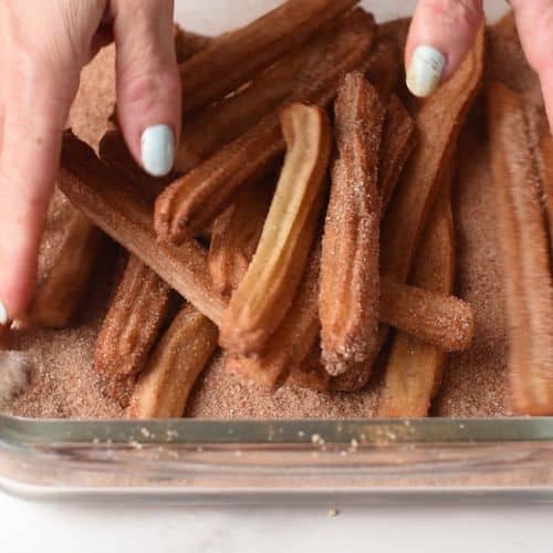 Tossing Baked Churros in cinnamon sugar.