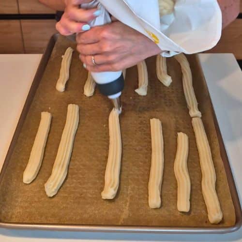 Piping churros on a baking sheet.