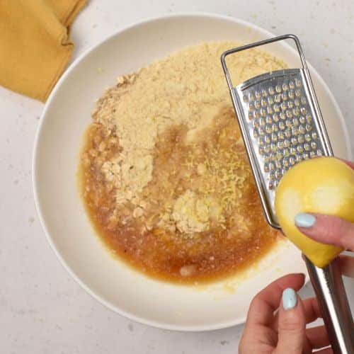 Grating lemon zest on the Lemon Oatmeal Cookie ingredients in a bowl.