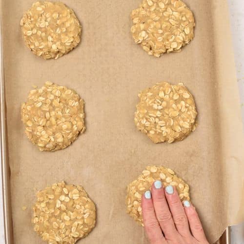 Flattening Lemon Oatmeal Cookies on a baking sheet.
