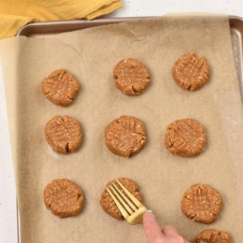 Forming criss-cross patterns on Oat Flour Peanut Butter Cookies on a baking sheet.