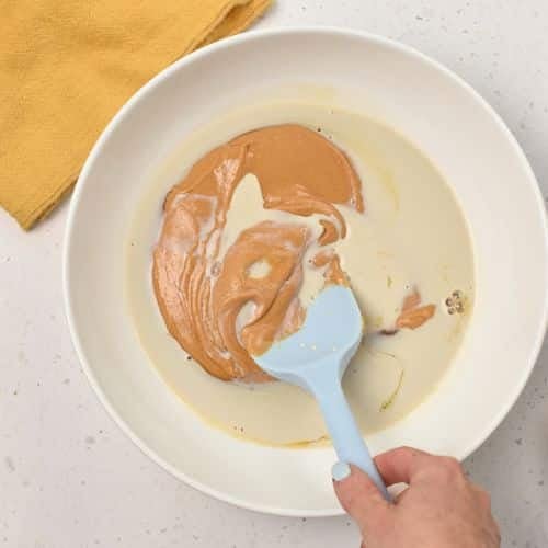 Combining almond milk and peanut butter into a bowl.