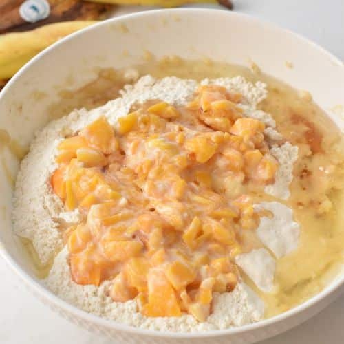 Adding peaches to Peach Banana Bread ingredients in a bowl.