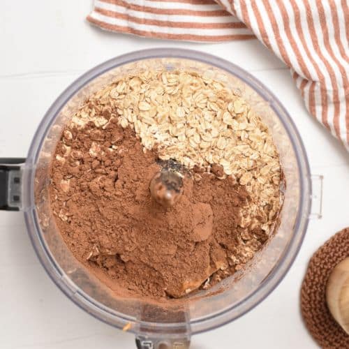 Adding oats and cocoa powder to a food processor.