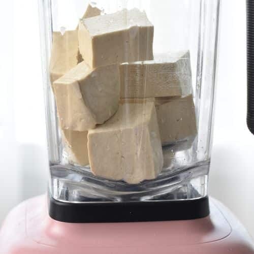 Adding blocks of tofu to a blender.